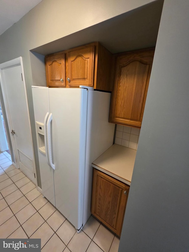 616 Sylvan Pl, Harrisburg, PA 17109 - kitchen with white refrigerator with ice dispenser, light tile patterned floors, brown cabinets, backsplash, and light countertops