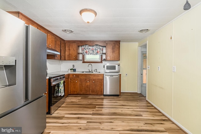 230 N Harrison St, Palmyra, PA 17078 - kitchen with appliances with stainless steel finishes, under cabinet range hood, a sink, light wood-style flooring, and brown cabinetry