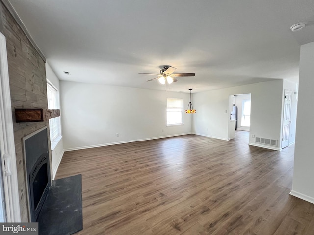 unfurnished living room with a large fireplace, ceiling fan, dark wood finished floors, and baseboards
