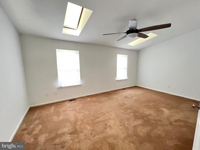 carpeted spare room featuring a skylight, baseboards, and ceiling fan