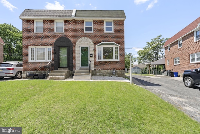 view of property with brick siding, a front yard, entry steps, and a shingled roof