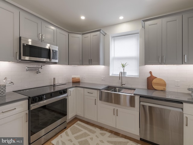 kitchen with stainless steel appliances, a sink, dark countertops, decorative backsplash, and recessed lighting