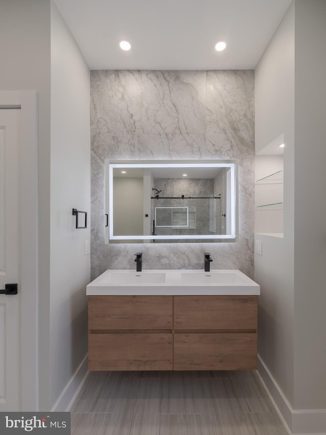 full bath featuring double vanity, a shower stall, baseboards, recessed lighting, and tile walls