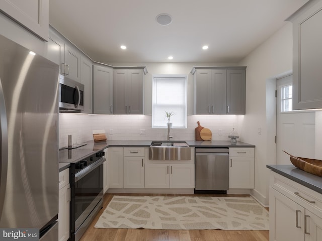 kitchen featuring appliances with stainless steel finishes, dark countertops, a sink, tasteful backsplash, and light wood-style floors