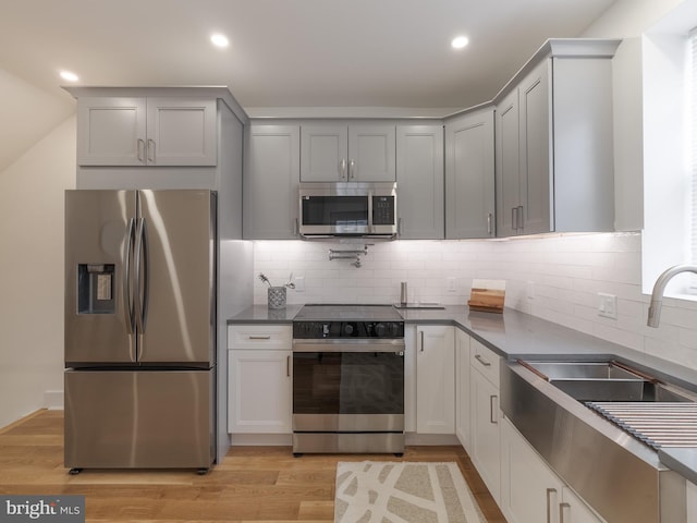 kitchen with stainless steel appliances, a sink, light wood-style flooring, dark countertops, and recessed lighting