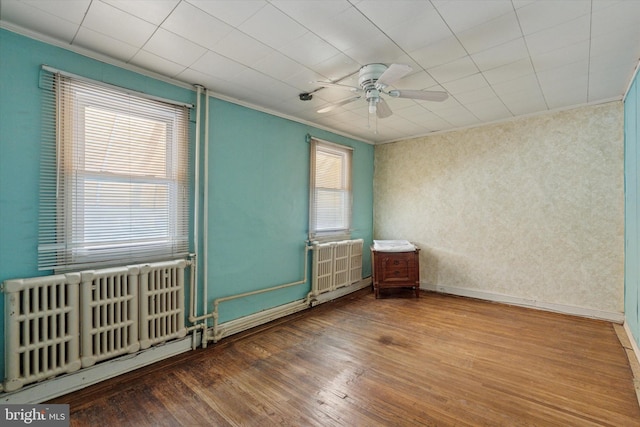 empty room with ornamental molding, hardwood / wood-style floors, a ceiling fan, radiator, and baseboards