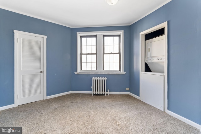 carpeted empty room featuring radiator, estacked washer and dryer, crown molding, and baseboards