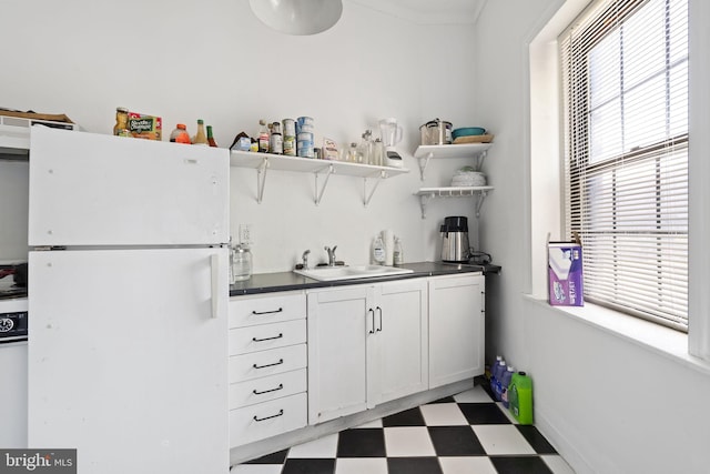 kitchen featuring freestanding refrigerator, a sink, light flooring, and plenty of natural light