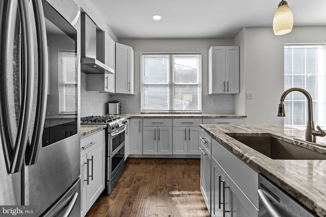 kitchen featuring stainless steel appliances, wall chimney range hood, a sink, light stone countertops, and recessed lighting