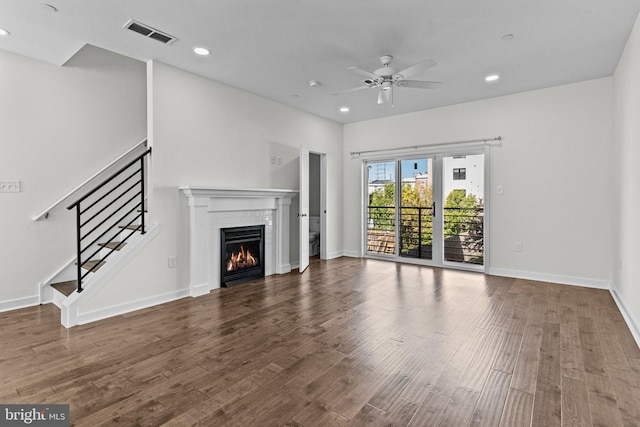 unfurnished living room with ceiling fan, recessed lighting, wood finished floors, a tile fireplace, and stairs