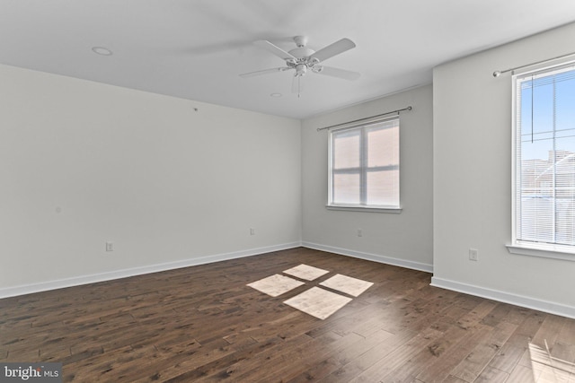 empty room featuring dark wood-type flooring, a ceiling fan, and baseboards