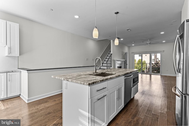 kitchen featuring a sink, stainless steel appliances, ceiling fan, open floor plan, and light stone countertops