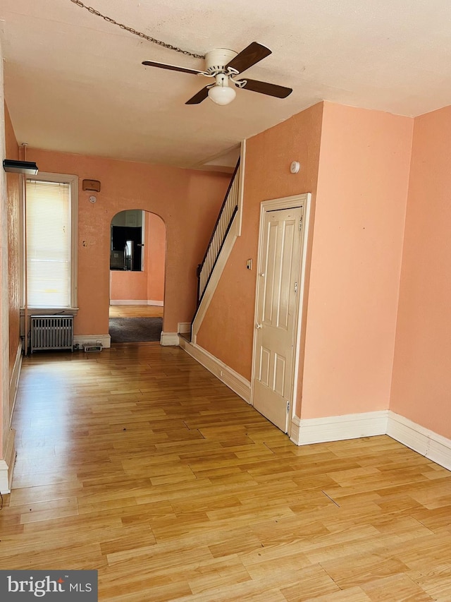 735 Locust St, Reading, PA 19604 - empty room with arched walkways, radiator, ceiling fan, stairway, and light wood-style flooring