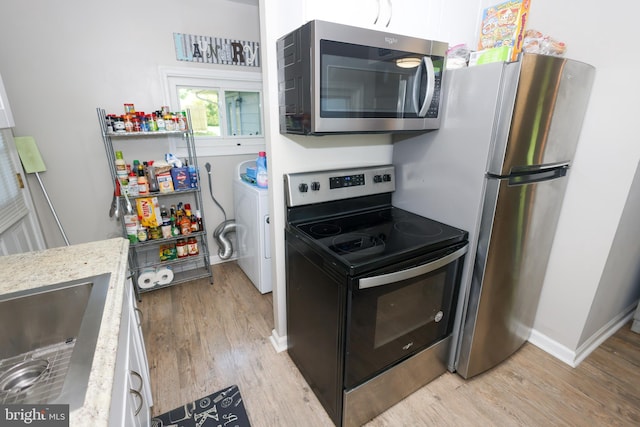 1675 Highland Ter, Saint Leonard, MD 20685 - kitchen with appliances with stainless steel finishes, washer / dryer, light wood-style floors, light stone counters, and white cabinets
