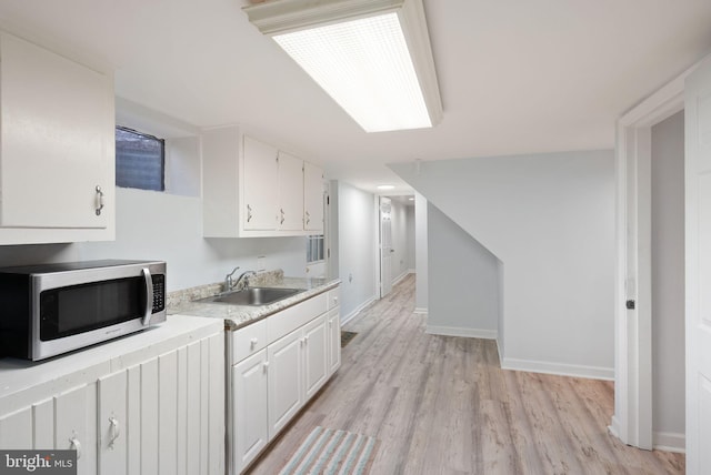 7434 Dickenson St, Springfield, VA 22150 - kitchen featuring stainless steel microwave, a sink, white cabinetry, light countertops, and light wood-style flooring