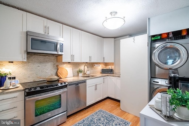 1600 N Oak St Unit 324, Arlington, VA 22209 - kitchen featuring appliances with stainless steel finishes, stacked washer and clothes dryer, a sink, white cabinets, and light wood-type flooring