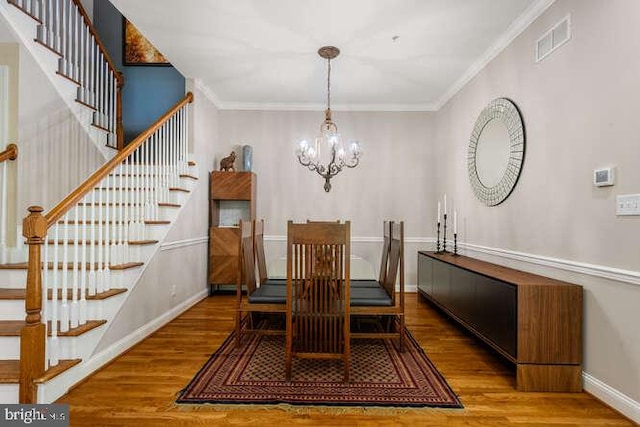 dining space featuring stairway, a chandelier, wood finished floors, ornamental molding, and baseboards