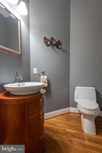 half bath with vanity, toilet, wood finished floors, and baseboards