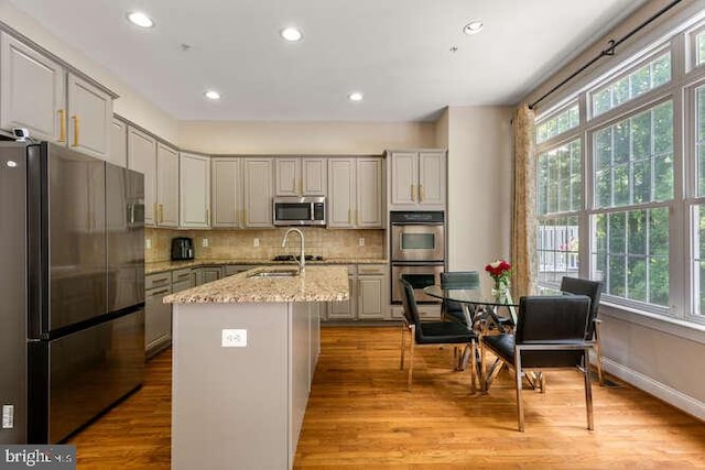 kitchen with stainless steel appliances, decorative backsplash, light stone counters, light wood-type flooring, and recessed lighting