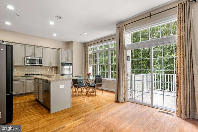 kitchen with stainless steel appliances, gray cabinets, a sink, light wood-type flooring, and decorative backsplash