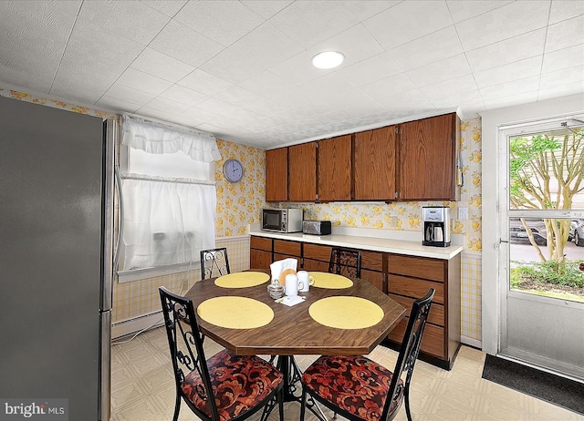 104 11th St, Ocean City, MD 21842 - kitchen with freestanding refrigerator, wallpapered walls, light flooring, brown cabinets, and light countertops