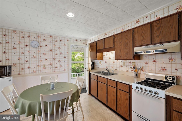104 11th St, Ocean City, MD 21842 - kitchen featuring under cabinet range hood, white gas stove, light flooring, light countertops, and a sink
