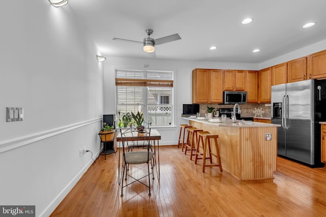 620 Cypress Ln, Severna Park, MD 21146 - kitchen featuring stainless steel appliances, a breakfast bar area, light wood-type flooring, a ceiling fan, and backsplash