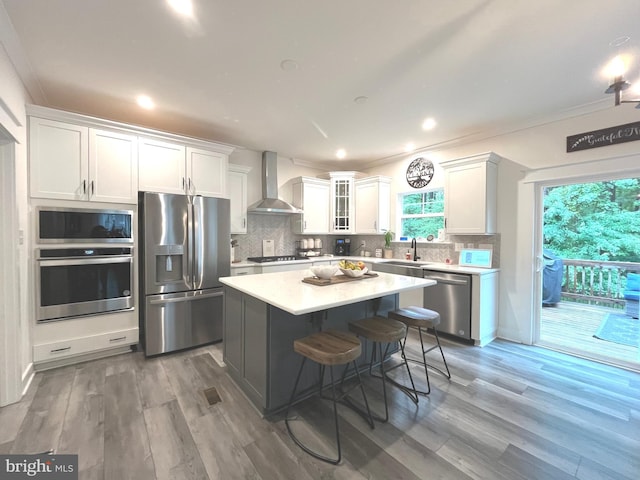 16801 Chalet Ct, Chesterfield, VA 23832 - kitchen with appliances with stainless steel finishes, wall chimney exhaust hood, white cabinets, a center island, and light wood finished floors
