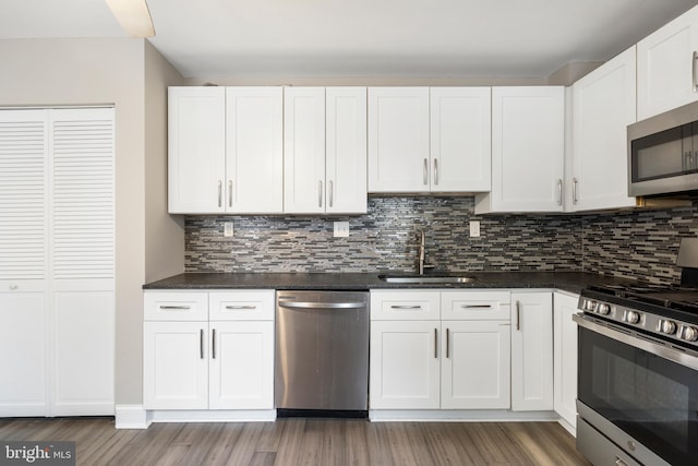 2808 Orleans St, Baltimore, MD 21224 - kitchen with appliances with stainless steel finishes, a sink, light wood finished floors, white cabinetry, and decorative backsplash