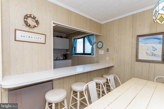 2901 Atlantic Ave Unit 404, Ocean City, MD 21842 - kitchen featuring crown molding, a kitchen breakfast bar, a textured ceiling, a sink, and wood walls