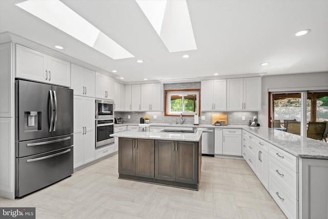10060 Hampton Rd, Fairfax Station, VA 22039 - kitchen featuring stainless steel appliances, a peninsula, a skylight, white cabinets, and tasteful backsplash