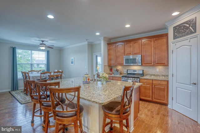 38623 Longs Chapel Ln, Millville, DE 19967 - kitchen featuring appliances with stainless steel finishes, a kitchen breakfast bar, light stone countertops, light wood-style floors, and crown molding