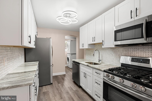 2032 S 21st St, Philadelphia, PA 19145 - kitchen featuring stainless steel appliances, a sink, stacked washing machine and dryer, arched walkways, and light wood-type flooring