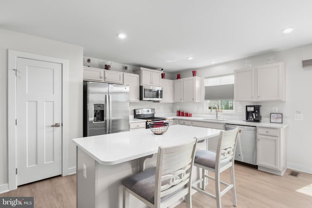 12037 Angora Dr, King George, VA 22485 - kitchen featuring appliances with stainless steel finishes, light wood finished floors, a kitchen island, a sink, and a breakfast bar area