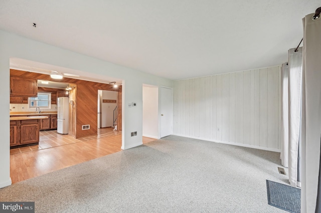 225 Dunlap Rd, Pasadena, MD 21122 - unfurnished living room with light colored carpet, wood walls, a sink, baseboards, and light wood finished floors