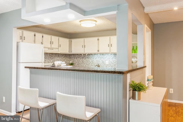 11833 Shire Ct Unit 12C, Reston, VA 20191 - kitchen with backsplash, a textured ceiling, light wood-type flooring, white cabinets, and under cabinet range hood