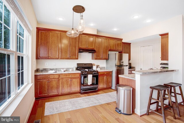 2505 Basin View Ln, Woodbridge, VA 22191 - kitchen featuring black gas range, freestanding refrigerator, under cabinet range hood, light wood-style floors, and brown cabinets