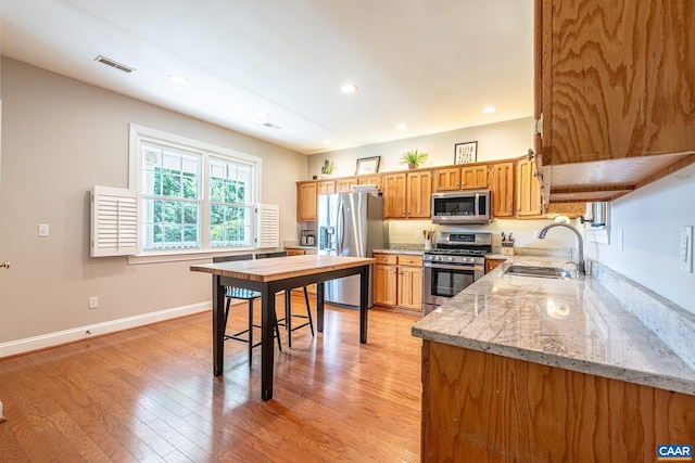 5301 Little Fox Ln, Charlottesville, VA 22903 - kitchen featuring appliances with stainless steel finishes, a sink, light wood-type flooring, brown cabinetry, and light stone counters