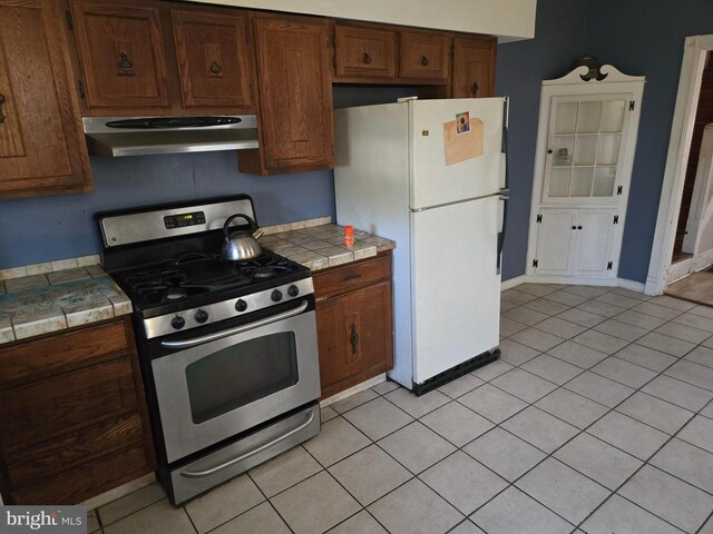 1151 E King St, York, PA 17403 - kitchen with stainless steel gas range, under cabinet range hood, freestanding refrigerator, tile counters, and light tile patterned floors