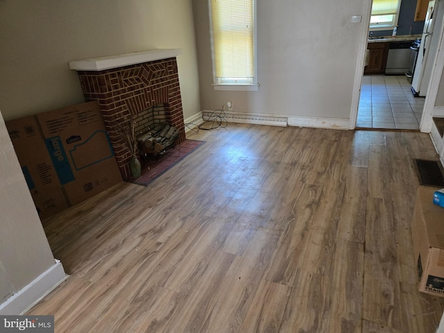 1151 E King St, York, PA 17403 - unfurnished living room with light wood-type flooring, a brick fireplace, baseboards, and a baseboard heating unit