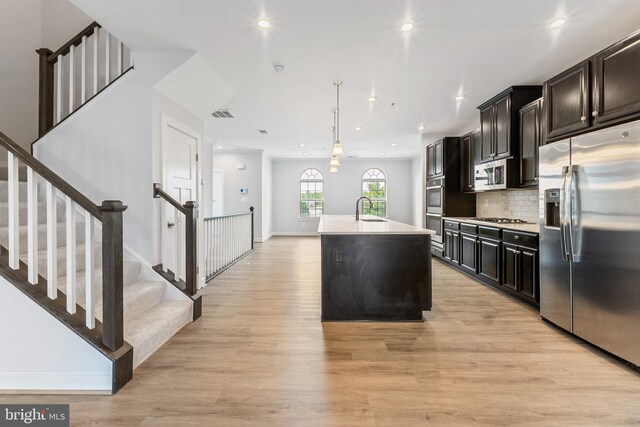 14438 Mattawoman Dr Unit 5000H, Brandywine, MD 20613 - kitchen with appliances with stainless steel finishes, a center island with sink, light wood-type flooring, light countertops, and decorative backsplash