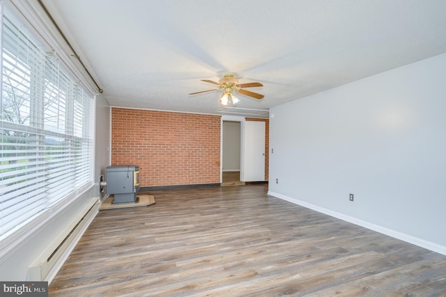 1267 Dominion Rd, Gerrardstown, WV 25420 - empty room with a wood stove, brick wall, ceiling fan, baseboard heating, and baseboards