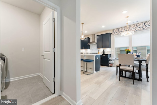 6411 Tulip Ter, Haymarket, VA 20169 - kitchen with wall chimney range hood, a kitchen bar, light countertops, baseboards, and tasteful backsplash