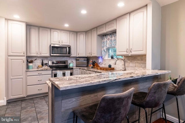 167 Windmill Rd, Willow Grove, PA 19090 - kitchen featuring appliances with stainless steel finishes, light stone countertops, a breakfast bar, tasteful backsplash, and recessed lighting