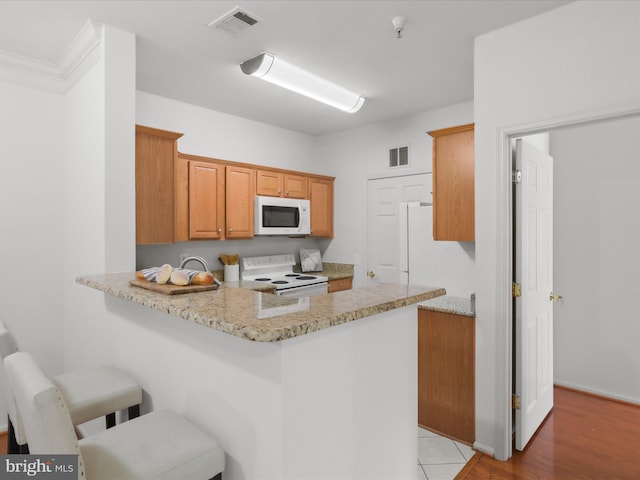 1521 Spring Gate Dr Unit 10308, Mclean, VA 22102 - kitchen featuring white appliances, a peninsula, light stone countertops, a kitchen bar, and baseboards