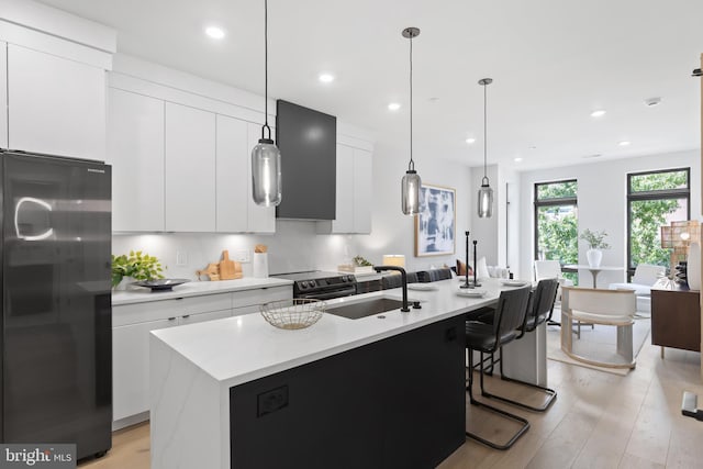 1208 M St NW Unit 52, Washington, DC 20005 - kitchen with freestanding refrigerator, light wood-style flooring, white cabinetry, a kitchen island with sink, and electric stove