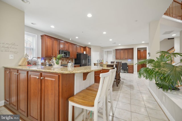 14201 Village Manor Ct, Upper Marlboro, MD 20774 - kitchen featuring stainless steel microwave, freestanding refrigerator, a peninsula, light stone countertops, and a kitchen breakfast bar