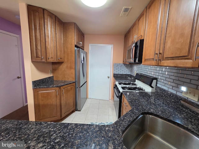 2704 Adams Ct, North Wales, PA 19454 - kitchen featuring appliances with stainless steel finishes, brown cabinets, tasteful backsplash, light tile patterned floors, and dark stone countertops