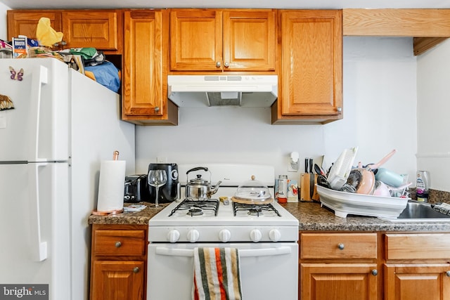 1227 Eddystone Ave, Crum Lynne, PA 19022 - kitchen with white appliances, under cabinet range hood, dark countertops, and brown cabinetry
