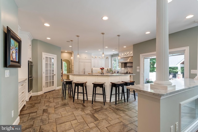 5026 Huntwood Manor Dr, Fairfax, VA 22030 - kitchen featuring ornate columns, under cabinet range hood, a kitchen breakfast bar, stone tile floors, and white cabinets
